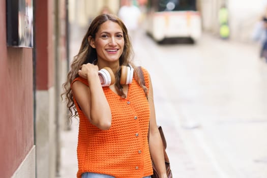 Latin beauty woman smiling walking in the city with headphones in her neck