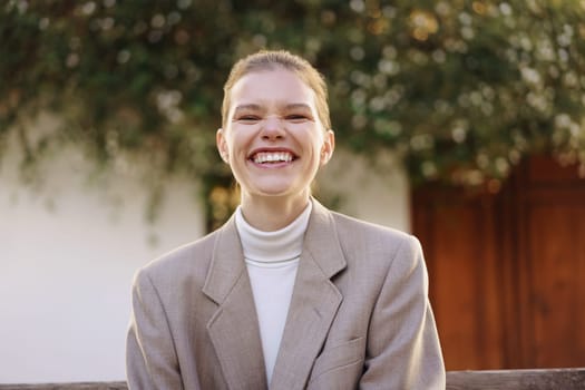 A joyful and energetic young woman dressed in a chic and fashionable outfit, proudly showcasing a bright and radiant smile set against a softfocus nature backdrop that enhances her cheerful demeanor