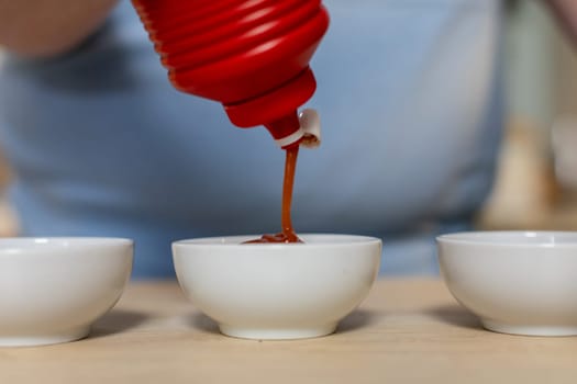 A closeup view of thick, rich ketchup being expertly poured into several small bowls for a meal or snack