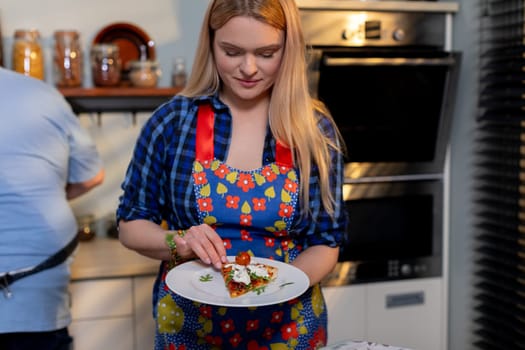 A woman dressed in a vibrant and colorful apron is meticulously plating a delicious dish in a modern kitchen setting