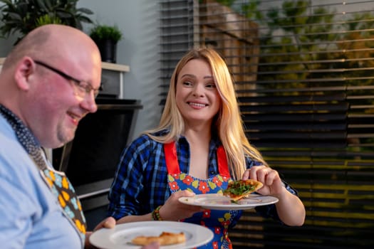 A cheerful duo joyfully sharing delicious food and hearty laughter in a warm and cozy kitchen atmosphere