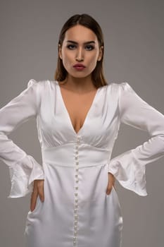 Confident female model wearing white shiny dress looking at camera studio portrait