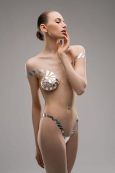 Portrait of slim woman with bra and panties made of metallic tape looking away against gray background