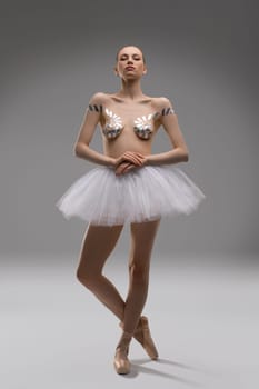 Attractive young slim female in ballet tutu skirt and with sticky tapes on breast posing in studio look at camera