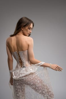 Confident seductive slim female model in translucent corset keeping hands on waist and undress peignoir