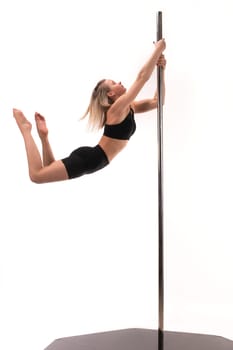Full body side view of young athletic gymnast in black gymnastic suit hanging on pole while performing acrobatic trick isolated white background