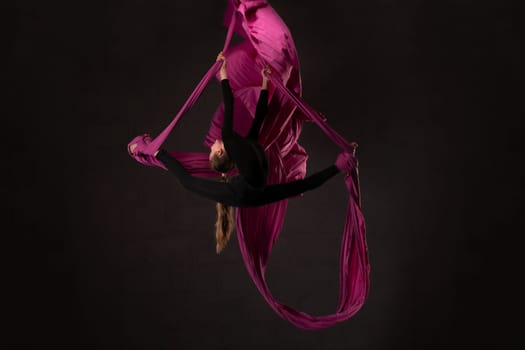 Full body side view of slim teem aerial silks performer doing acrobatic splits while hanging on purple fabric against white background