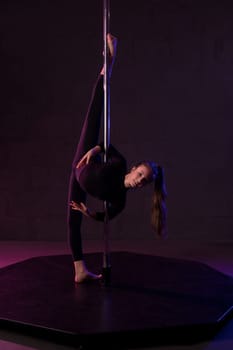 Full body of flexible young female gymnast in leotard performing acrobatic standing splits near pole in dark studio