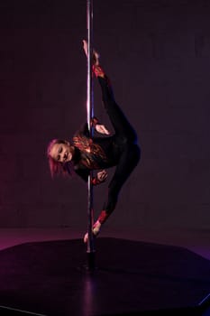 Full body of flexible teen female gymnast in leotard performing acrobatic standing splits near pole in dark studio