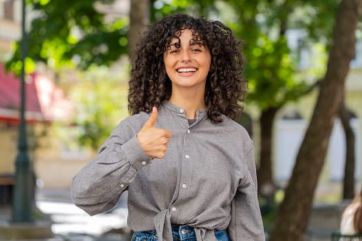Like. Happy Caucasian young woman raises thumbs up agrees with something gives positive reply recommends advertisement good idea feedback, celebrating success victory outdoors. Guy on city street.