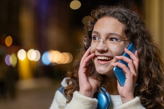 Phone call, good news, gossip. Happy amazed Caucasian teenage girl in pleasant conversation on smartphone, enjoying talking with friend outdoors. Tourist in city street at night. Town lifestyles