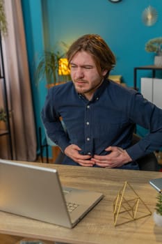 Disappointed freelancer feeling overeating during work process on laptop in home office. Upset businessman freelancer guy man touching stomach and experiencing discomfort and sharp pain. Vertical
