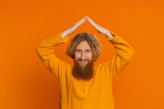 House roof about head. Caucasian man playing childish catching up game, feeling in safe making roof above head with hands, insurance, security service. Redhead young guy isolated on orange background