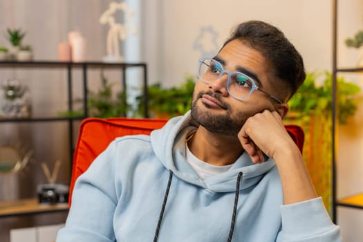 Portrait of sad Indian Hindu man guy sits at home looks pensive thinks over life concerns or unrequited love, suffers from unfair situation. Problem, break up, depressed feeling bad annoyed, burnout