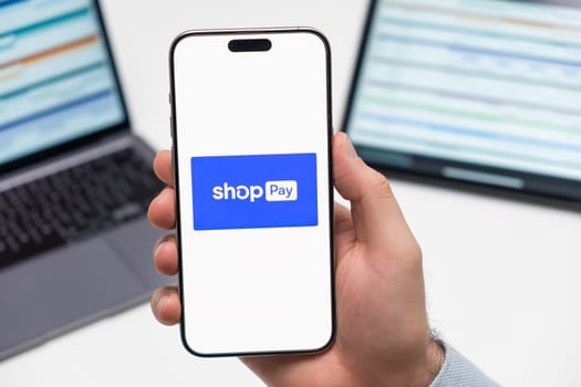 PRAGUE, CZECH REPUBLIC - JANUARY 21 2024: Shop pay logo on the screen of smartphone in mans hand on the workplace background.