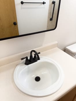 Broomfield, Colorado, USA-January 25, 2025-A stylish bathroom vanity featuring a large rectangular mirror with a black frame, a white sink with a black faucet, and a beige countertop. The vanity is complemented by a three-light fixture above the mirror, providing ample lighting. A black towel bar is mounted on the wall, enhancing the modern design. The bathroom has a clean, minimalist look with neutral tones and functional elements.