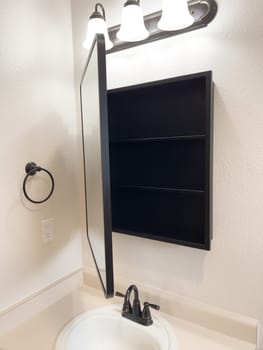 Broomfield, Colorado, USA-January 25, 2025-A stylish bathroom vanity featuring a large rectangular mirror with a black frame, a white sink with a black faucet, and a beige countertop. The vanity is complemented by a three-light fixture above the mirror, providing ample lighting. A black towel bar is mounted on the wall, enhancing the modern design. The bathroom has a clean, minimalist look with neutral tones and functional elements.