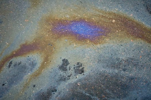 Colorful oil slick reflecting a spectrum of colors on the fissured asphalt road