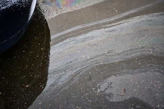 Gasoline or oil spill creating rainbow sheen on asphalt parking lot near car.
