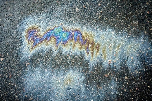 Gasoline or oil spill on asphalt creating rainbow sheen reflecting light