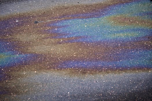 Gasoline rainbow creating colorful pollution on wet asphalt road
