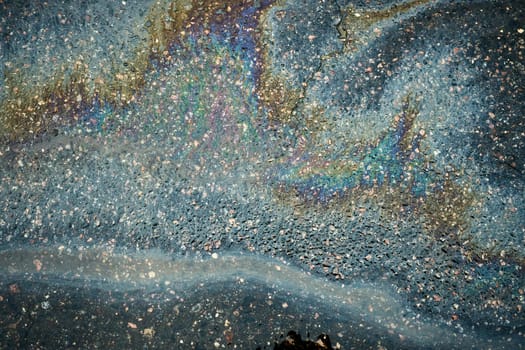 Gasoline rainbow sheen flows towards storm drain on asphalt