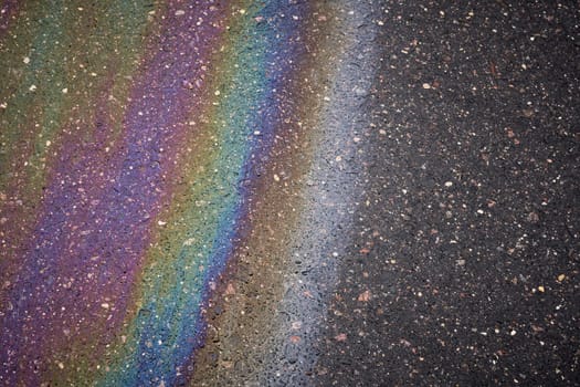 Gasoline spill creating rainbow sheen on asphalt road surface