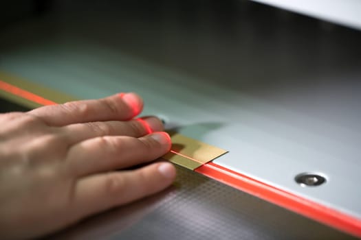 Crop unrecognizable female fingers on laser line of modern digital paper cutting machine in workshop
