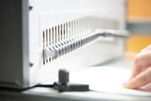 Crop unrecognizable female employee using manual bookbinder machine while creating new notebook in workshop
