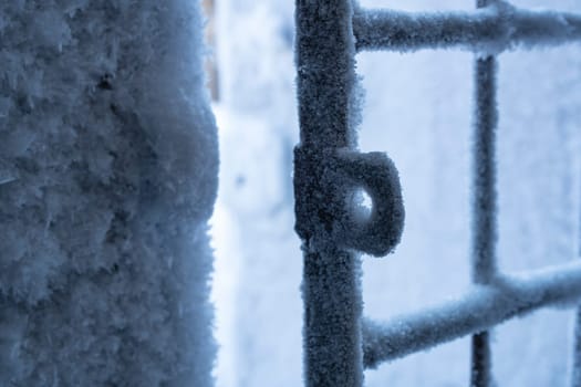 Closeup of open metal grating fence covered by white hoarfrost in cold winter day