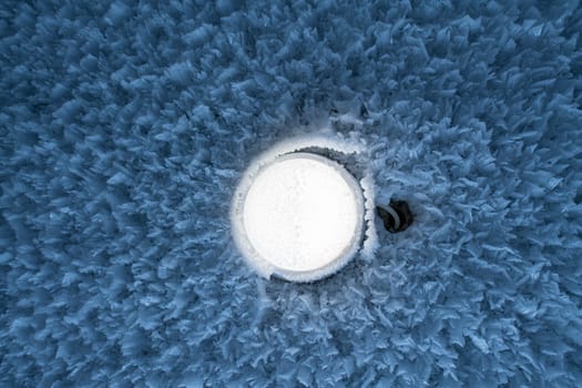 Closeup of round shaped lamp shining on frozen wall covered with white hoarfrost in wintertime