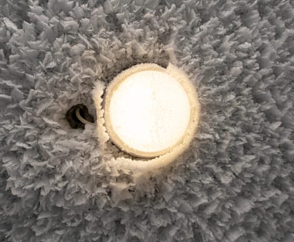 Closeup of round shaped lamp shining on frozen ceiling covered with white hoarfrost in frozen wintertime