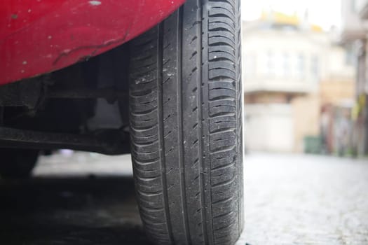 A red car tire rests on a rocky surface in an urban area.