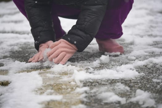 Child kneels in snow, using gloved hands to touch the cold surface.