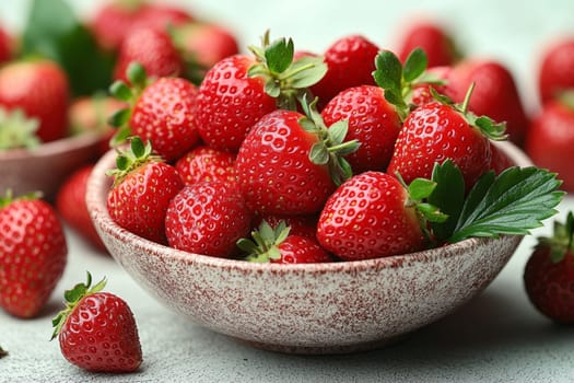Bright red strawberries are piled in a rustic bowl, showcasing their vibrant color and freshness on a textured surface.