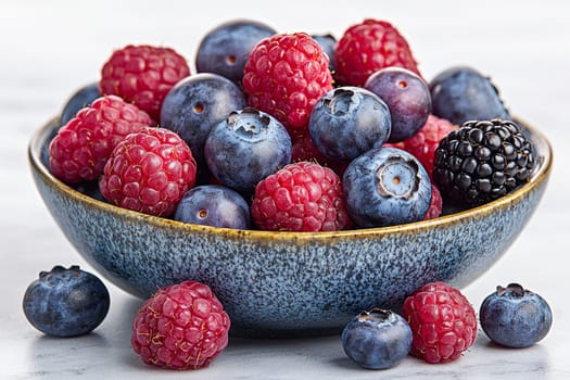 Fresh berries including raspberries, blueberries, and blackberries are beautifully arranged in a bowl, showcasing vibrant colors.