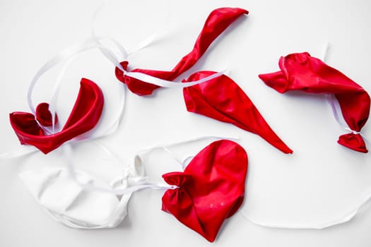 Deflated red and white balloons with ribbons on white background.