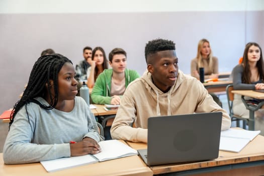 Multi ethnic students listening to lesson in university classroom, using laptop and taking notes