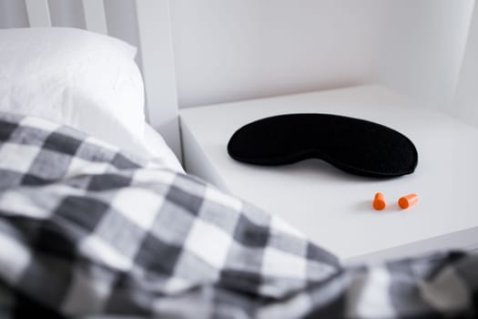 Cozy bedroom with sleep mask and earplugs on nightstand in soft light.