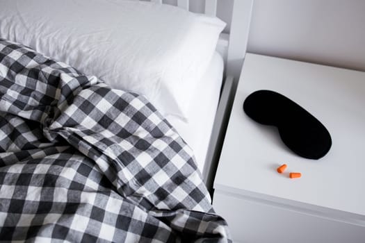 Cozy bedroom scene with black and white plaid blanket and sleep accessories on nightstand.