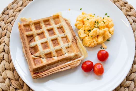 Breakfast plate with ham and cheese toast, scrambled eggs, and tomatoes.