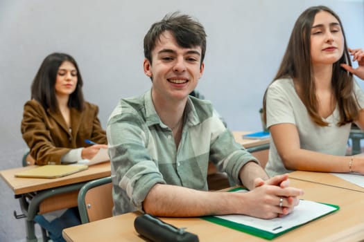 Portrait of a cheerful male student sitting at desk in classroom, attending a lesson at high school, college or university