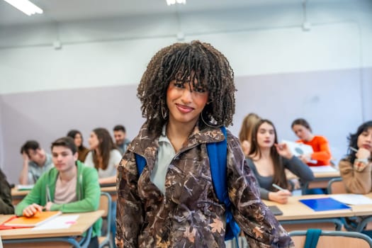 Confident young university student standing in classroom with backpack, classmates studying in background, higher education concept