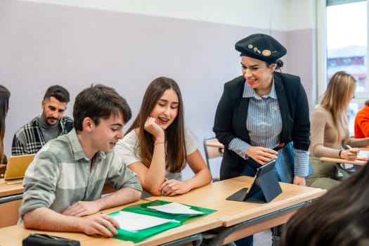 University teacher using tablet explaining lesson to two students sitting at desk in classroom