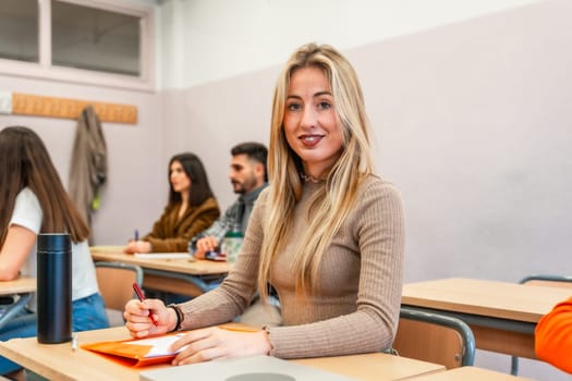 Blonde female college student taking notes and engaging in learning during a university lesson in a focused classroom environment