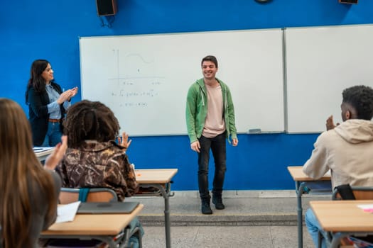 Happy college student explaining lesson at whiteboard while professor and classmates applaud him in modern classroom