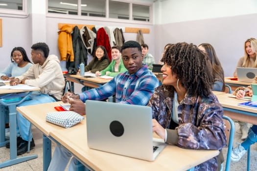 Multi ethnic university students are collaborating on a project using a laptop in a classroom, engaging in teamwork and learning