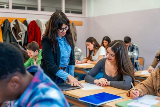 Female professor assisting a smiling student with her exam paper in a classroom full of diverse students taking a test