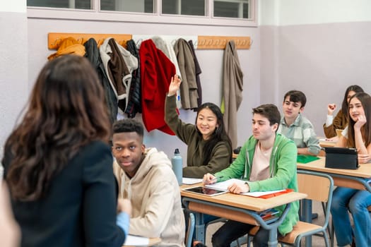 Multi ethnic group of high school students attending a lesson, a girl is raising her hand to ask a question to the teacher