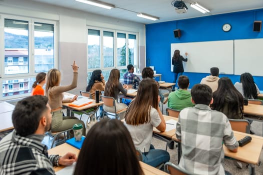 Multi ethnic university students listening to their teacher and raising their hand to answer a question in a classroom